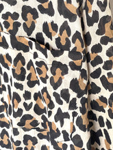 Load image into Gallery viewer, Close-up of a leopard print fabric with black, brown, and tan spots on a cream background, showing a pocket seam and texture.