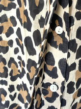Load image into Gallery viewer, Close-up of a leopard print fabric garment with black, tan, and cream spots, showing part of a buttoned front closure.