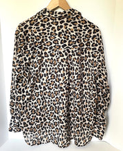 Load image into Gallery viewer, A leopard print long-sleeve blouse hanging on a wooden hanger against a plain white wall.