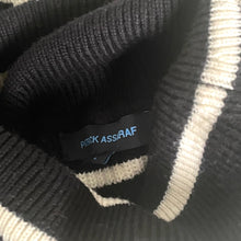 Load image into Gallery viewer, Close-up of a sweater with a brand label on a textured fabric background