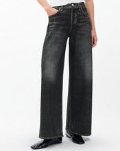 Load image into Gallery viewer, A person wearing dark gray wide-leg denim jeans with a faded wash, paired with black patent leather shoes against a plain white studio background.
