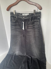 Load image into Gallery viewer, Dark gray washed denim flare jeans hanging on a wooden hanger against a white wall, with a paper tag still attached.