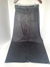 Load image into Gallery viewer, A pair of wide-leg denim jeans in a faded black wash, shown from the back hanging on a wooden hanger against a white background.