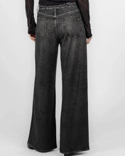 Load image into Gallery viewer, Back view of a person wearing wide-leg black washed denim jeans with a sheer black long-sleeve top, against a light gray studio background.