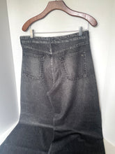 Load image into Gallery viewer, Dark gray washed denim jeans hanging on a wooden hanger against a plain white wall, showing the back pockets and waistband.