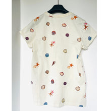 Load image into Gallery viewer, White t-shirt with colorful shell pattern on a hanger against a white background