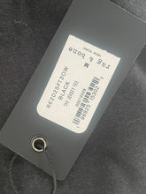 Load image into Gallery viewer, Clothing tag with product details on a dark fabric background