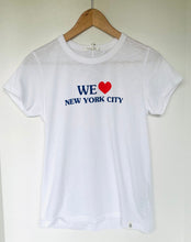 Load image into Gallery viewer, A white short-sleeve crewneck t-shirt hanging on a wooden hanger against a plain off-white wall. The shirt features a graphic print on the chest reading 'WE' in blue, a red heart, and 'NEW YORK CITY' in blue.
