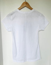 Load image into Gallery viewer, A plain white short-sleeve crewneck t-shirt hanging on a wooden hanger against a light off-white wall.