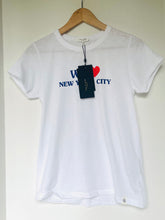 Load image into Gallery viewer, A white short-sleeve crewneck t-shirt hanging on a wooden hanger against a plain off-white wall. The shirt features a graphic print on the chest with the text 'WE NEW YORK CITY' in blue and a red heart.