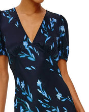 Load image into Gallery viewer, A close-up of a model wearing a navy blue wrap-style dress with a light blue floral print, featuring short puff sleeves and a deep V-neckline.