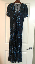 Load image into Gallery viewer, A black midi-length dress with a blue floral pattern, hanging on a wooden hanger against a white paneled door.