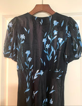 Load image into Gallery viewer, A black sheer mesh dress with a light blue floral and leaf pattern, hanging on a wooden hanger against a white door.