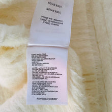 Load image into Gallery viewer, Fabric tag with washing instructions on a textured beige background