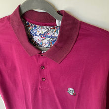 Load image into Gallery viewer, Pink polo shirt with skull design on a hanger