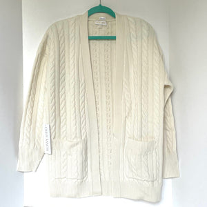 Cream-colored cable knit cardigan on a hanger against a white background