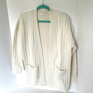 Beige cable knit cardigan on a hanger against a white background