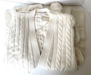 Stack of white cable knit sweaters on a white background