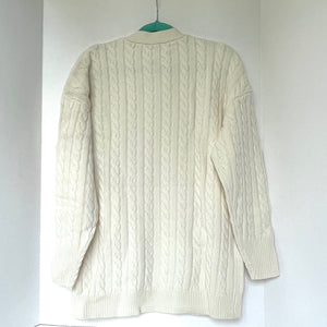 Cream-colored cable knit sweater on a white background