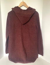 Load image into Gallery viewer, A ribbed knit hooded sweater in a deep burgundy or maroon color, hanging on a wooden hanger against a plain white wall.
