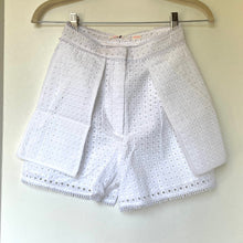 Load image into Gallery viewer, White eyelet shorts with a textured geometric pattern, hanging on a wooden hanger against a plain off-white wall.