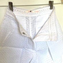 Load image into Gallery viewer, White textured eyelet fabric garment, likely a skirt or shorts, hanging from metal clips on a horizontal bar against a light background.