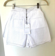 Load image into Gallery viewer, White eyelet shorts hanging from a hanger with a paper tag that reads 'sassy &amp; fine', set against a plain off-white wall.