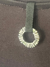 Load image into Gallery viewer, A close-up of a silver-tone metal ring charm with the word 'SWEAT' repeated around the circle, attached to a dark gray fabric strap on a dark gray ribbed garment.