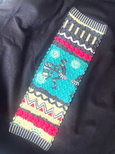 Load image into Gallery viewer, A close-up of a colorful embroidered fabric sleeve or patch with geometric patterns and a central dancer motif, laid on a black garment.