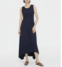 Load image into Gallery viewer, A woman wearing a sleeveless black and white horizontally striped midi dress with a high-low hem and brown sandals, standing against a plain white background.