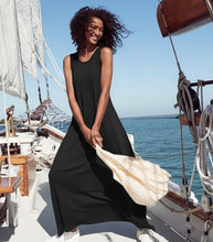 Load image into Gallery viewer, A woman stands on a sailboat deck wearing a sleeveless navy and white striped maxi dress, holding a large cream-colored beach bag against a background of blue sky and sea.