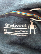 Load image into Gallery viewer, Close-up of the inner neck label of a dark gray knit garment, showing the brand 'Smartwool' with size 'XS' and 'Women/Femmes' printed in white, alongside a small robot logo.