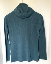 Load image into Gallery viewer, A dark teal long-sleeve athletic top with a high mock neck, hanging on a wooden hanger against a plain white wall.