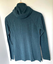 Load image into Gallery viewer, A dark teal long-sleeve athletic top with a high mock neck, hanging on a wooden hanger against a plain white wall.