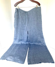 Load image into Gallery viewer, Blue wide-leg pants hanging on a wooden hanger against a white background