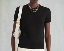 Load image into Gallery viewer, Person wearing a black sweater with a white bag and gold necklace on a light gray background