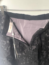 Load image into Gallery viewer, Close-up of a black patterned jacket or coat hanging on a metal hanger, showing a light lavender-gray interior lining and a sewn-in price tag that reads 'SARAI ANAHO'.