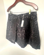 Load image into Gallery viewer, A black and gray floral jacquard skirt hanging on a wooden hanger against a plain white wall, with a paper tag attached.
