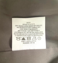 Load image into Gallery viewer, A close-up of a white garment care label sewn onto a dark gray fabric surface.