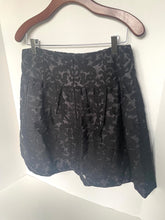 Load image into Gallery viewer, A black and gray floral jacquard skirt hanging on a wooden hanger against a white wall.