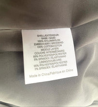 Load image into Gallery viewer, A close-up of a white fabric care label sewn onto the inside of a taupe-gray garment, showing text including 'Made in China' and material composition.