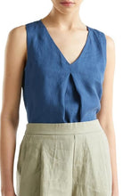 Load image into Gallery viewer, A woman wearing a sleeveless blue V-neck top with a gathered front and light olive green high-waisted pants, shown from the neck down against a plain white background.