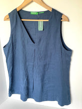 Load image into Gallery viewer, A sleeveless slate blue linen vest with a V-neckline, hanging on a wooden hanger against a plain white wall. The brand name 'The Artisanal Shop' is visible on the green neck labels.