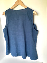 Load image into Gallery viewer, A sleeveless slate blue linen top hanging on a wooden hanger against a plain off-white wall.