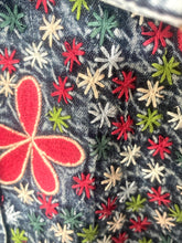 Load image into Gallery viewer, Close-up of a dark denim fabric with colorful embroidered starbursts in red, green, white, and beige, plus a large red flower motif outlined in light beige.