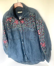 Load image into Gallery viewer, A blue denim button-up shirt jacket with pink and red embroidered butterfly motifs and a small white floral pattern across the chest and sleeves, hanging on a wooden hanger against a plain off-white wall.
