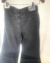 Load image into Gallery viewer, Back view of a pair of faded black denim jeans hanging on a wooden hanger against a white wall.