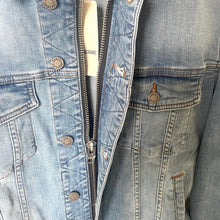 Load image into Gallery viewer, Close-up of a blue denim jacket with visible branding and details.