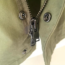 Load image into Gallery viewer, Close-up of a green jacket zipper with a brand tag on a light background