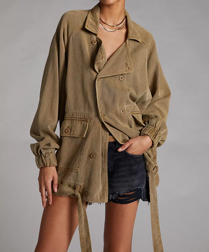 Person wearing a brown jacket and denim shorts on a gray background